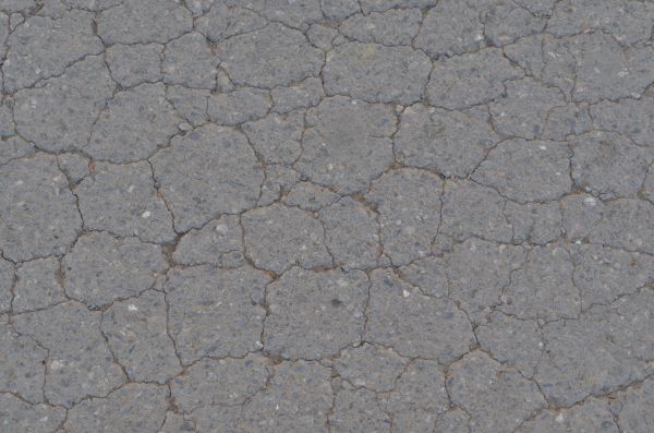 Coarse grey asphalt texture, with large deep cracks in its surface.